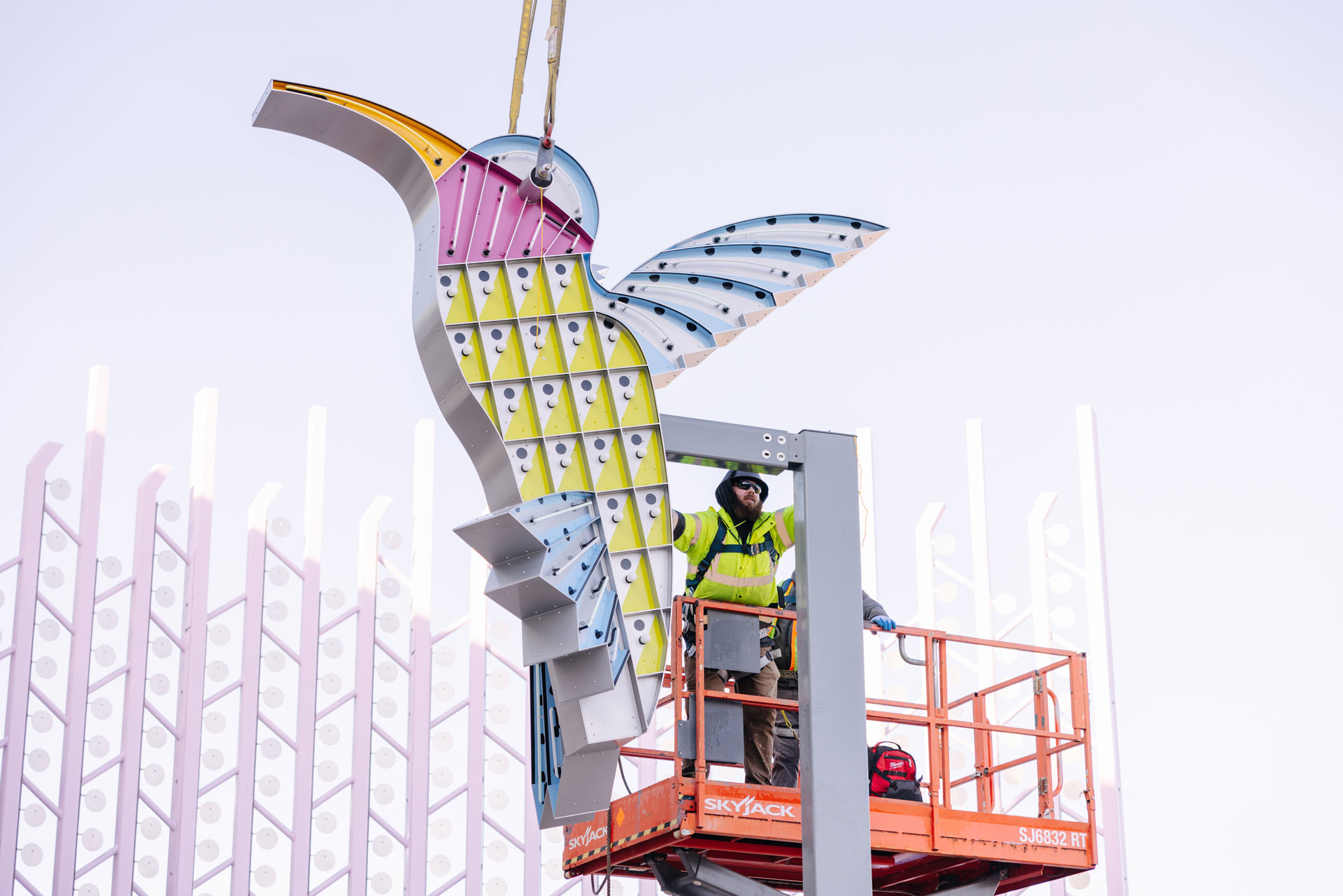 Un trabajador de la construcción sobre un elevador hidráulico da los toques finales en una nueva instalación de arte de un colorido colibrí iluminado con luces de neón en el Centro de Transporte Público de Lynwood.  