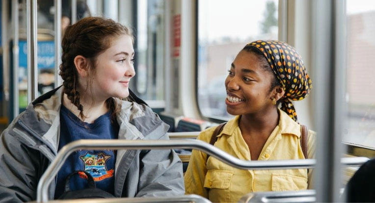 Dos adolescentes caminan con sus bicicletas por una plataforma de Link light rail con un tren en el fondo.  
